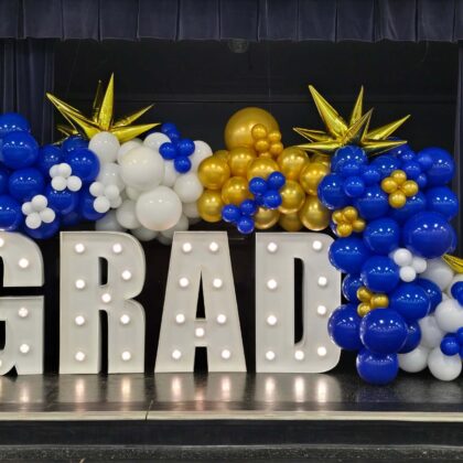 Graduation-themed balloon display with 'GRAD' letters on a stage.