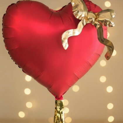 Red heart-shaped balloon with a gold ribbon against a blurred light background