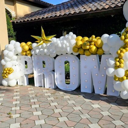 Decorative setup with 'PROM' letters surrounded by balloons on a stone patio.